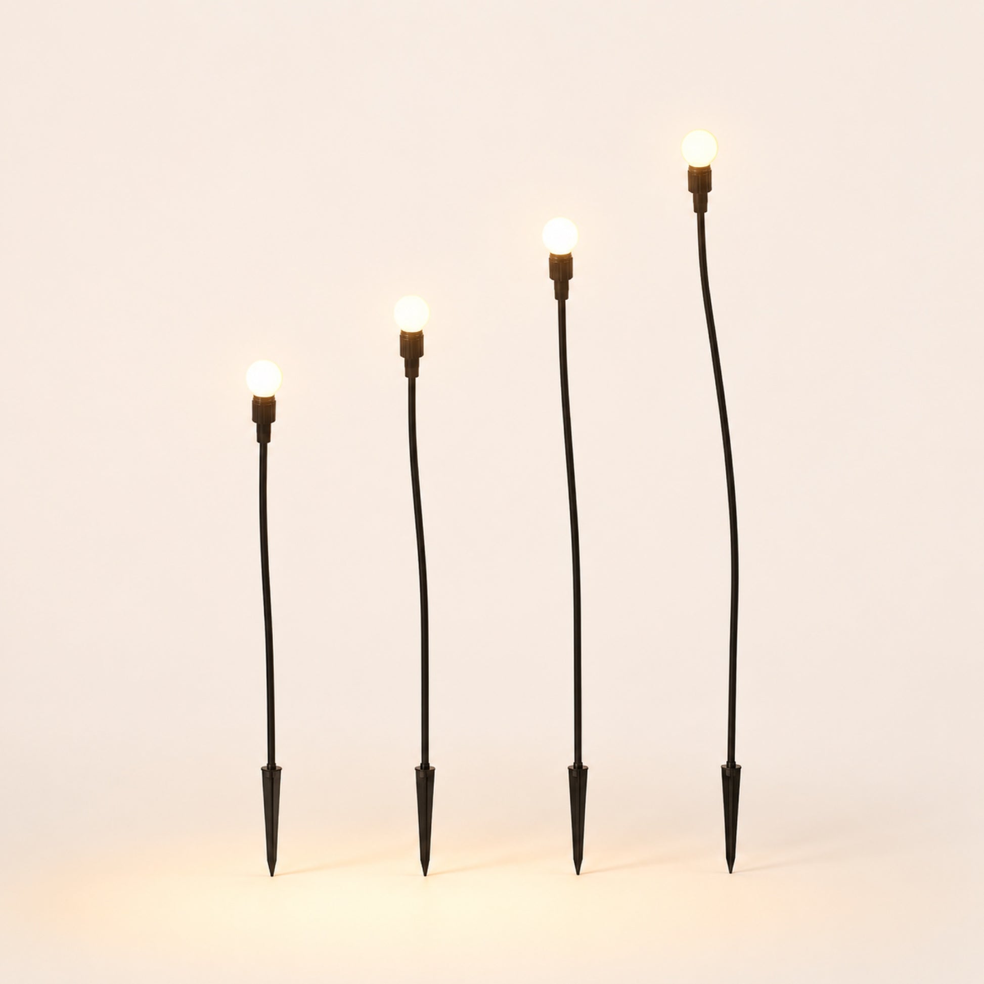 The Firefly Set: four solar garden stakes with warm glowing bulbs on porcelain background