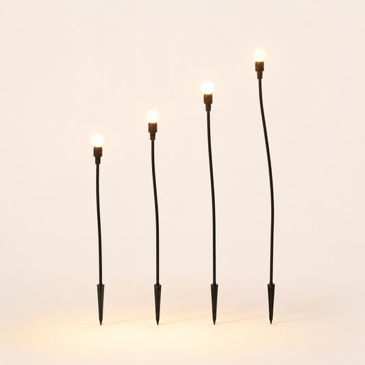 The Firefly Set: four solar garden stakes with warm glowing bulbs on porcelain background