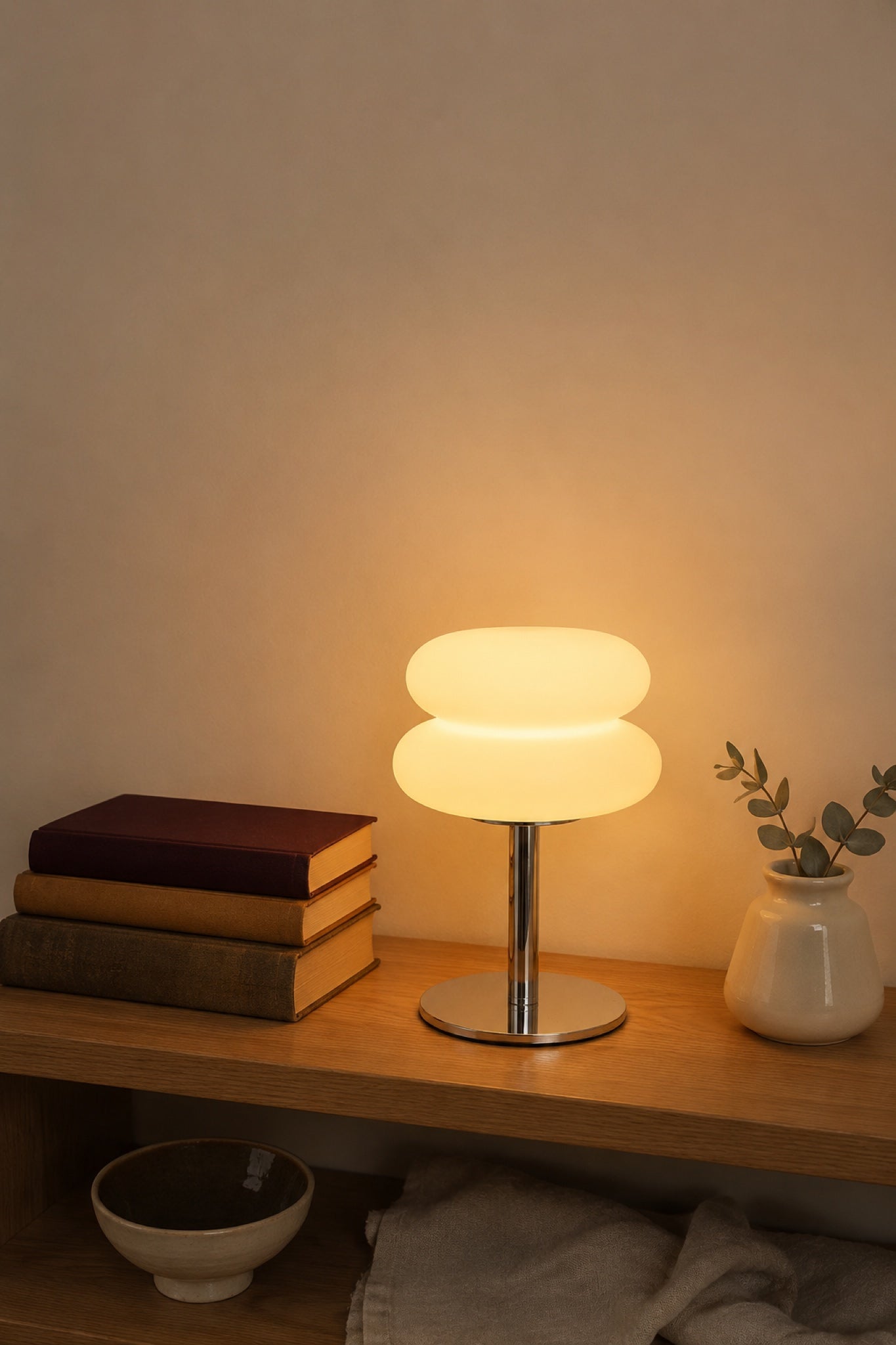 The Mushroom lamp glowing on an oak shelf between vintage books and a ceramic vase