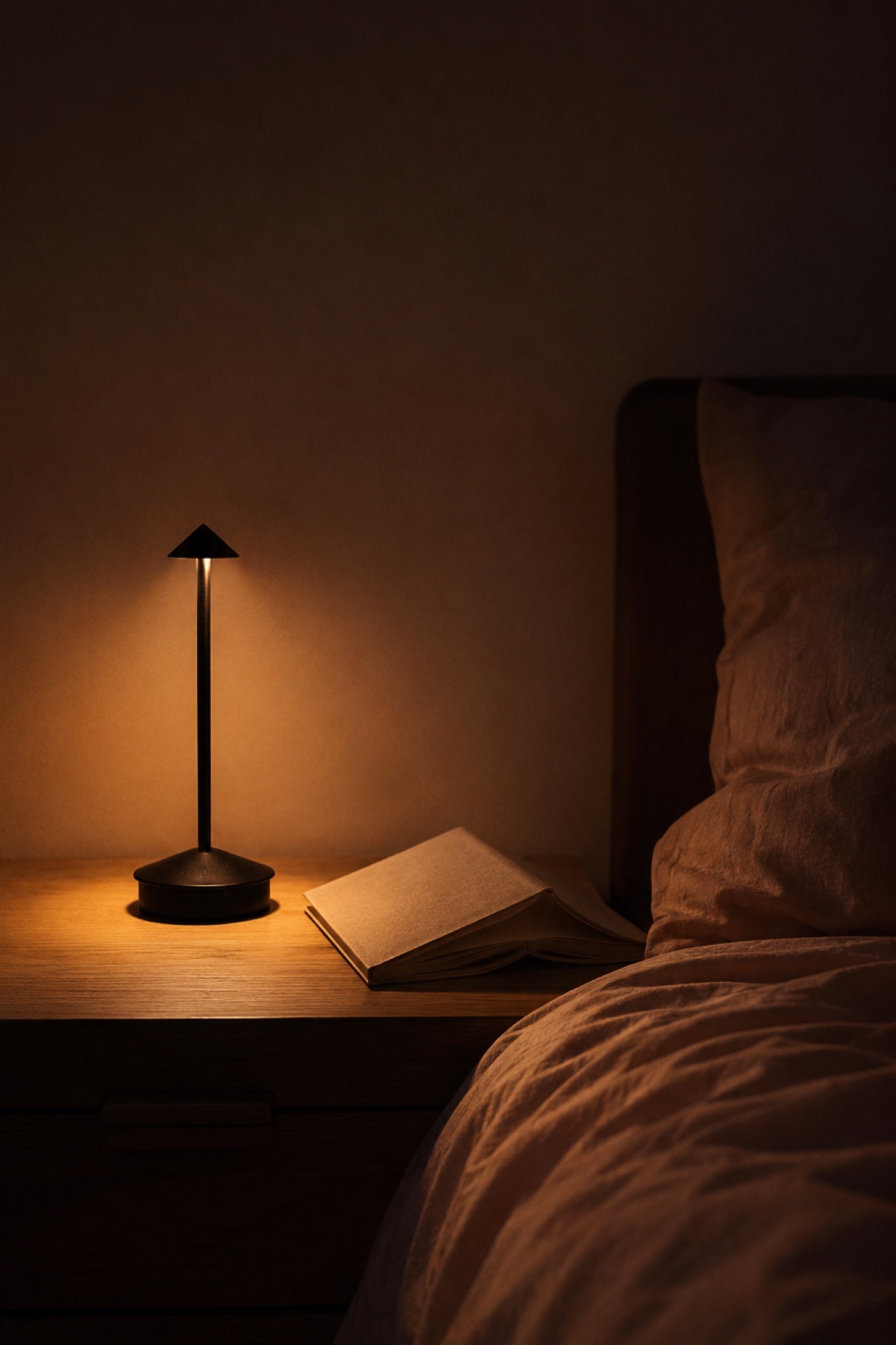 The Wren in matte black glowing on a bedside table next to an open book