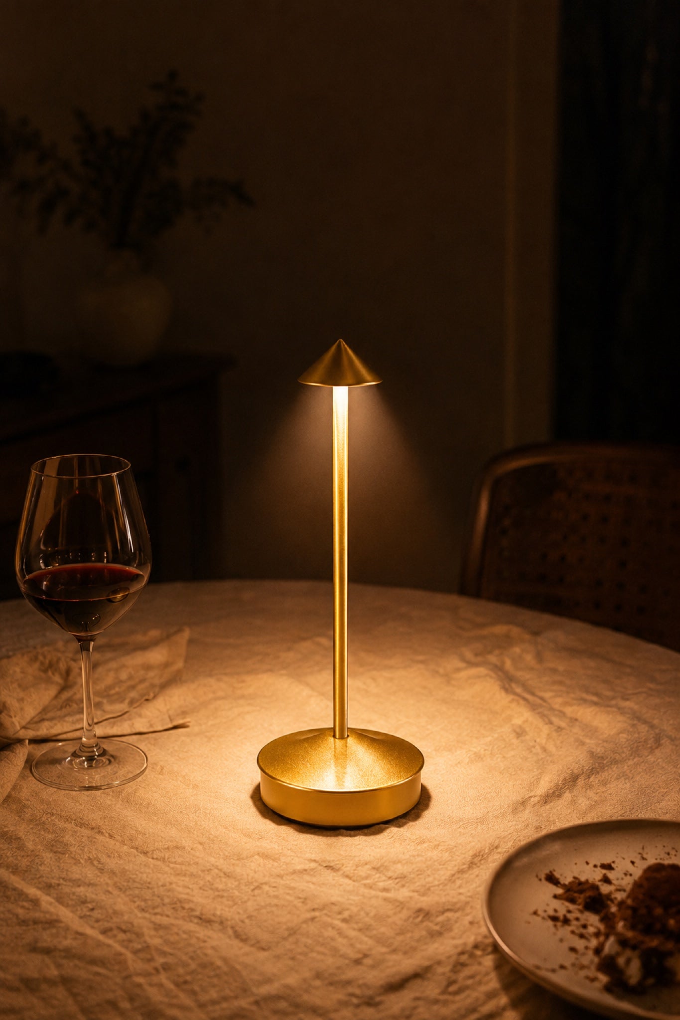 The Wren cordless lamp in brass gold glowing on a linen dinner table at night