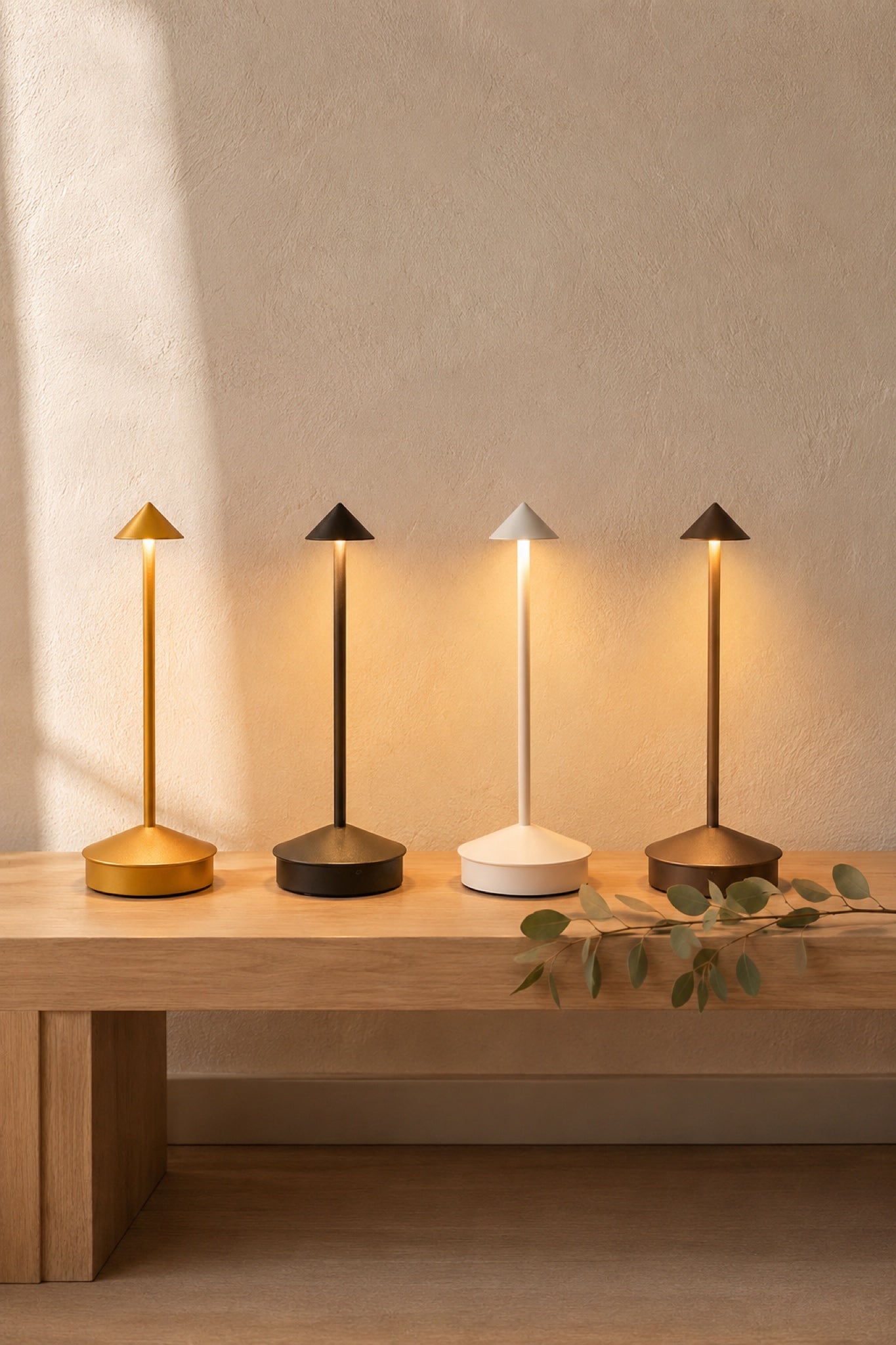 All four Wren finishes lit in a row on an oak bench: brass gold, matte black, soft white, bronze